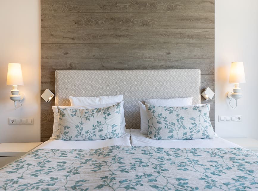 Double bed with a green floral bedspread, upholstered headboard and wall lights