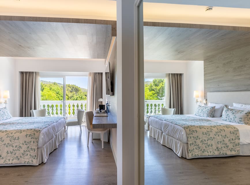 View of the double room reflected in the mirror, with bed, desk and a balcony overlooking greenery