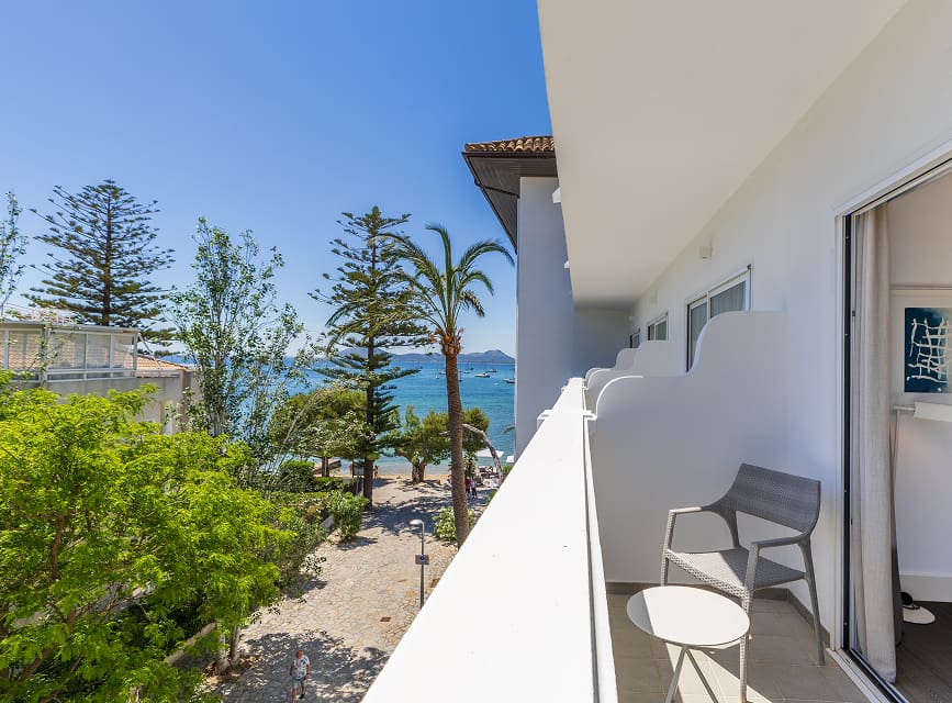 Balcony with chair and table overlooking the gardens, pine trees and the sea at Puerto Pollensa