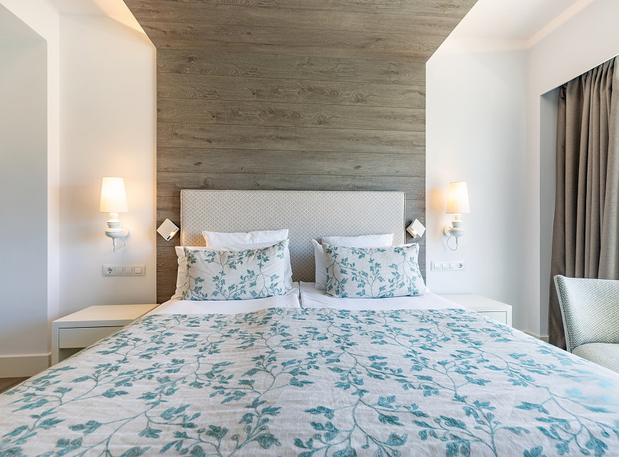 Standard room with a double bed, green floral bedspread, wood-panelled wall and wall lights