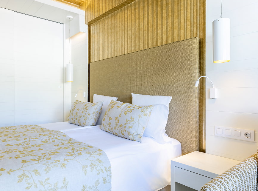 Beds with a golden floral bedspread, upholstered headboard and reading light in the standard room