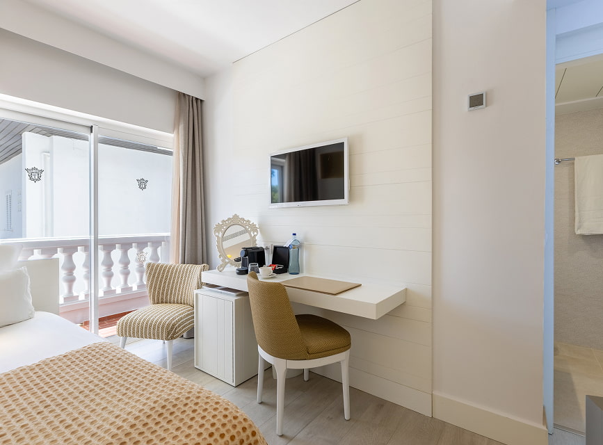 Single room with bed, desk, TV, armchair and door to the balcony