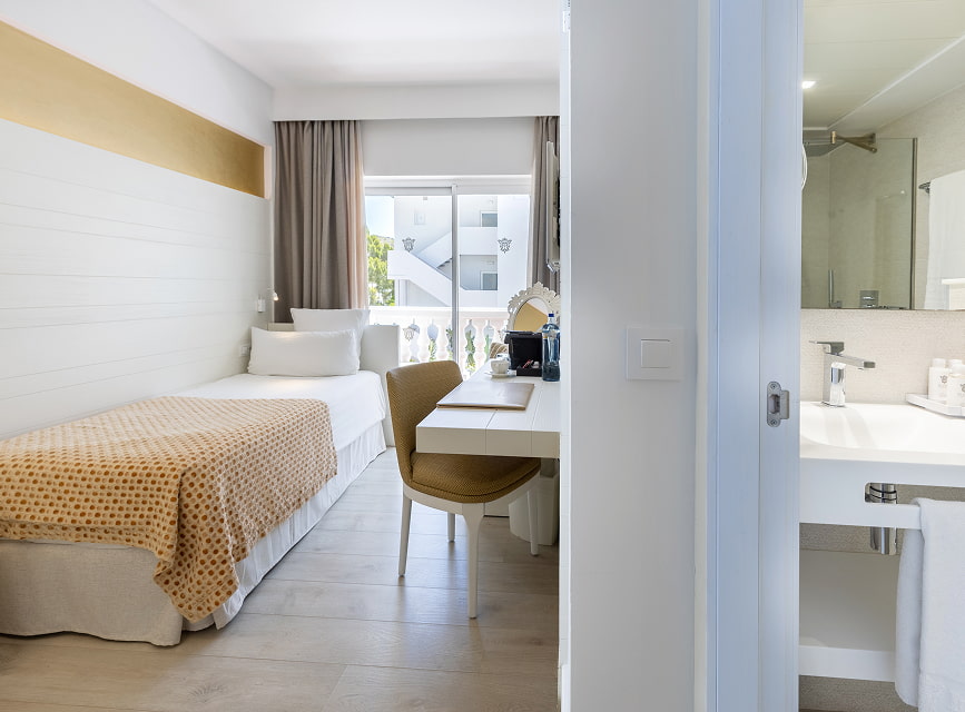 Single room with bed, desk and bright window, with the shower bathroom on the right