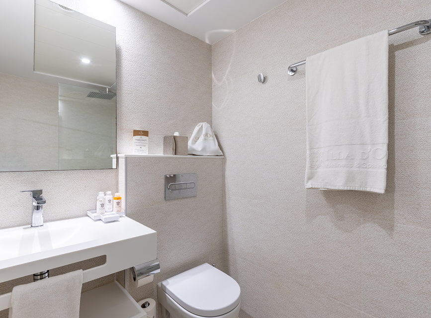 Bathroom with wall-hung washbasin, mirror, toilet and white towels with the hotel logo