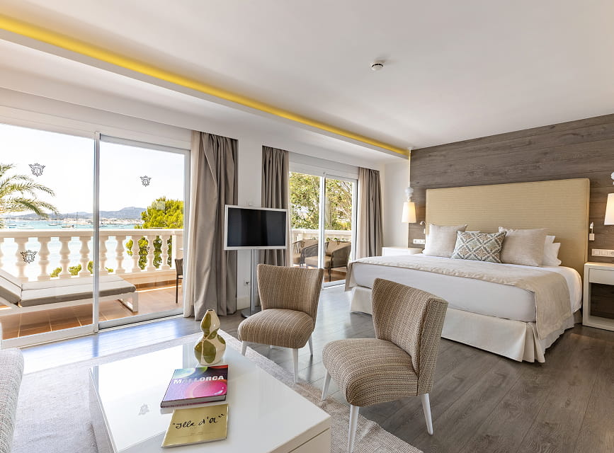 Spacious suite with double bed, seating area and large windows opening onto a terrace overlooking Pollensa Bay