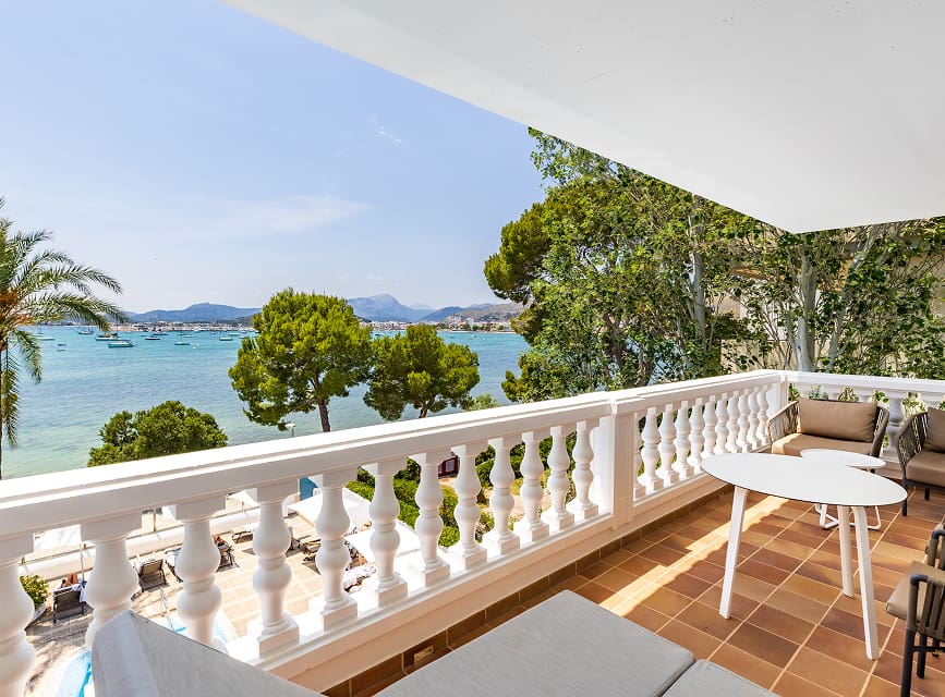 Private suite terrace with table, chairs and armchairs, overlooking Pollensa Bay through the pines
