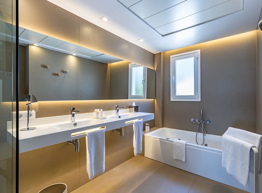 Suite bathroom with hydromassage bathtub, double washbasin, illuminated mirror and white towels