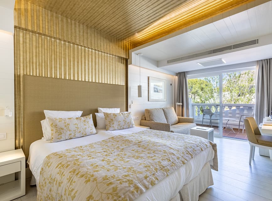 Room with twin beds pushed together, floral bedspread, sofa seating area and a balcony with side sea views