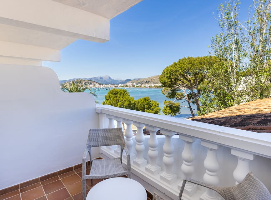 Balcony with chairs and table offering side views of Pollensa Bay through the pines, with mountains beyond