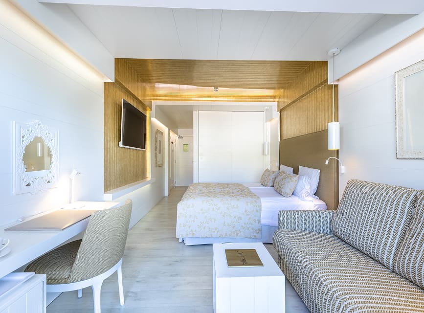 Room with double bed, upholstered sofa, desk, TV and classic-style mirror
