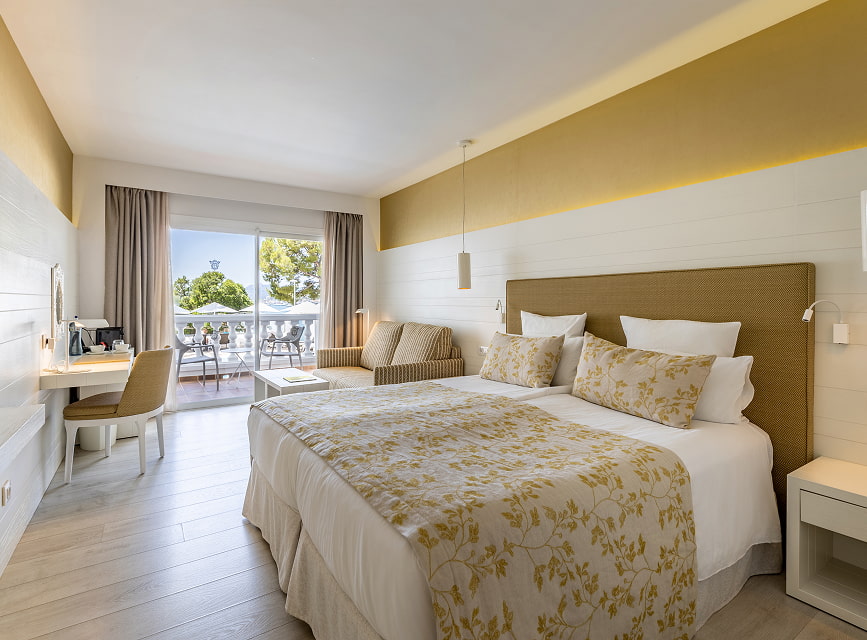 Bright room with twin beds pushed together, floral bedspread, desk, sofa and balcony access