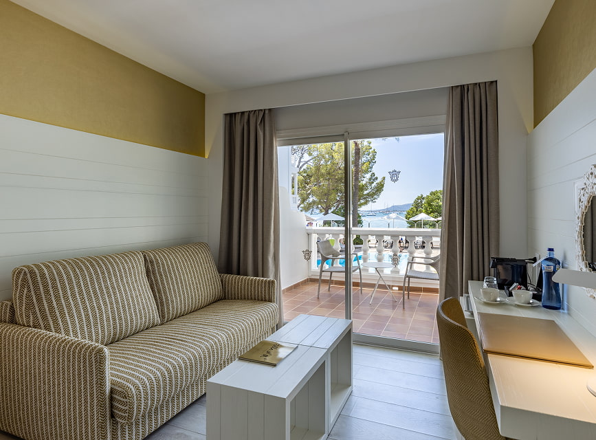Seating area with sofa, desk with coffee maker and a glass door to the sea-view balcony
