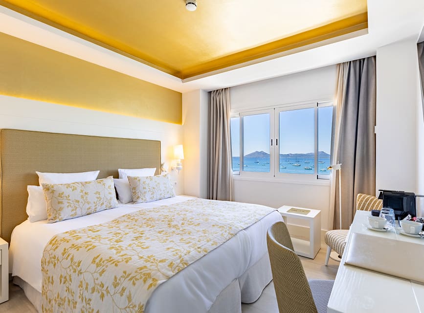 Room with double bed, floral bedspread, illuminated golden ceiling and a window with sea views