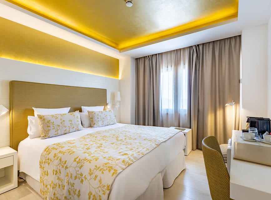 Room with a double bed with floral bedspread, upholstered headboard and neutral-toned curtains