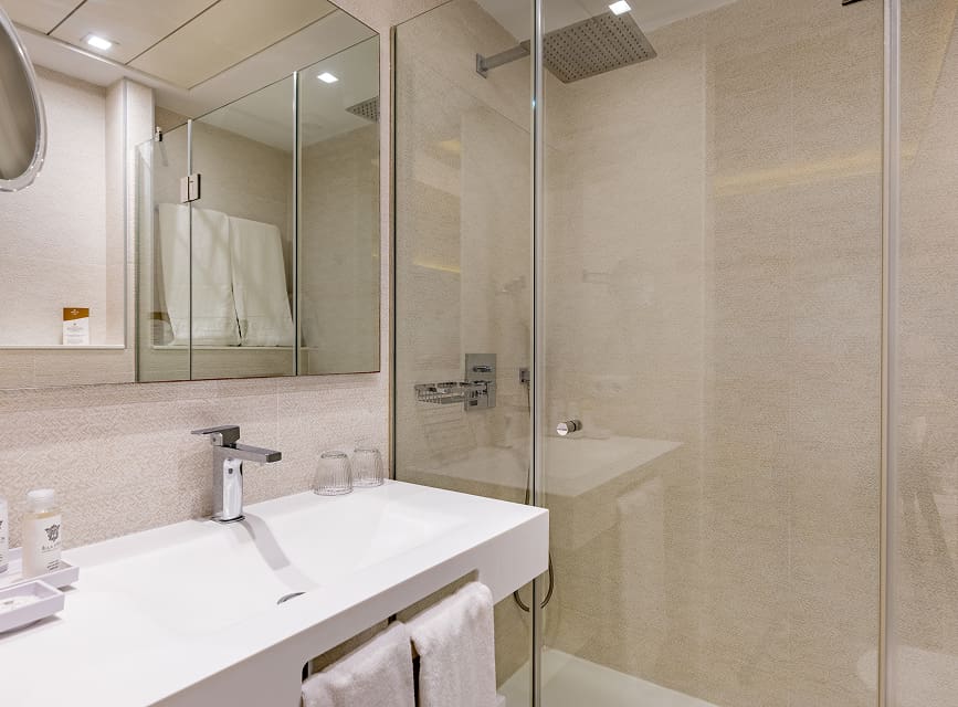 Bathroom with glass rain shower, washbasin, mirror and towels in the Sea view room